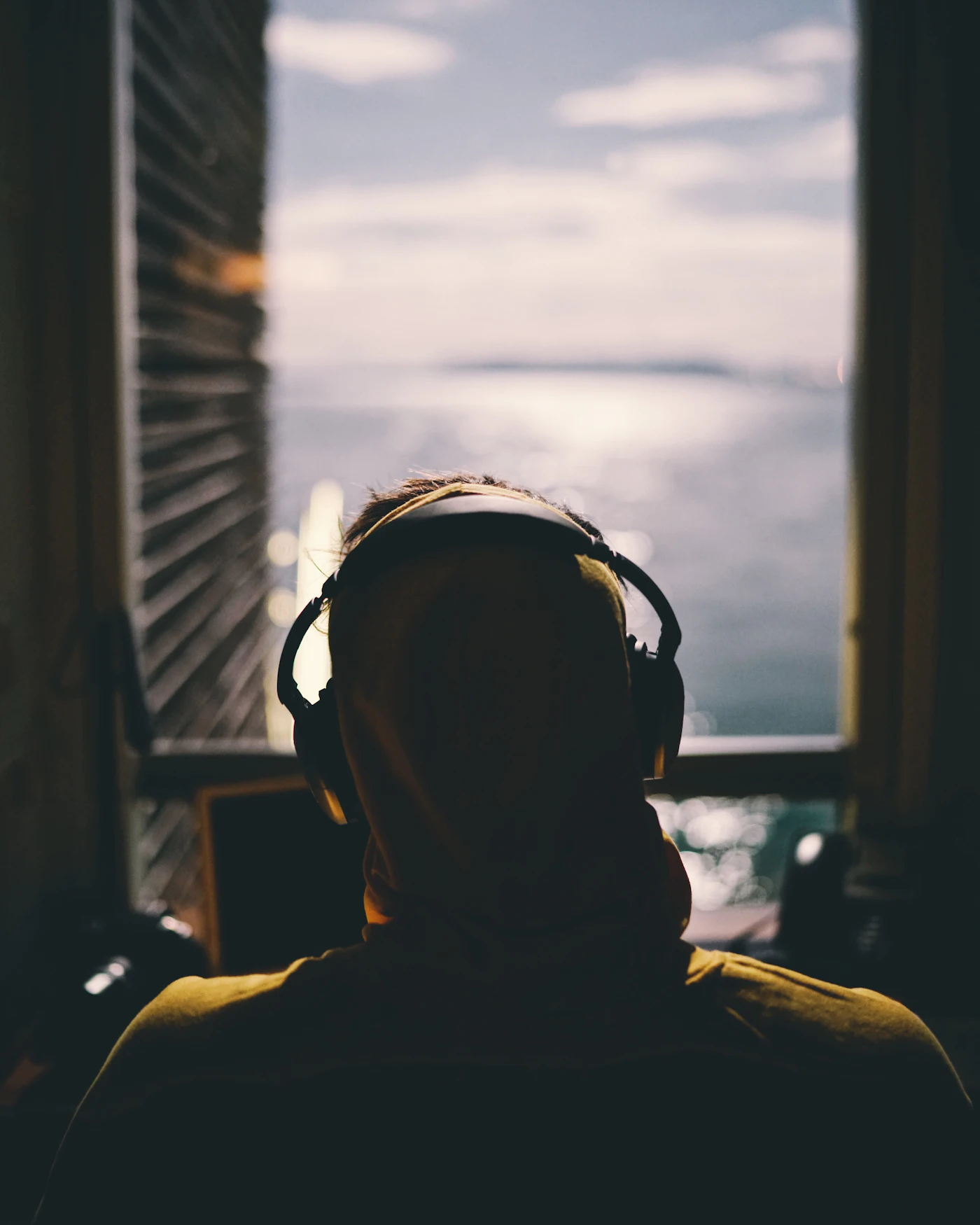 Someone with headphones on, looking out of a window at the sea